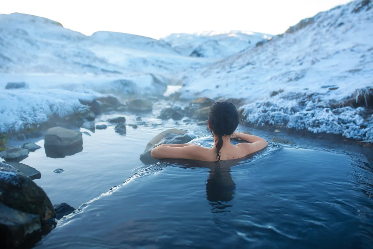 Visitantes relajándose en las humeantes fuentes termales geotermales de Islandia, rodeados de exuberantes paisajes verdes en julio.