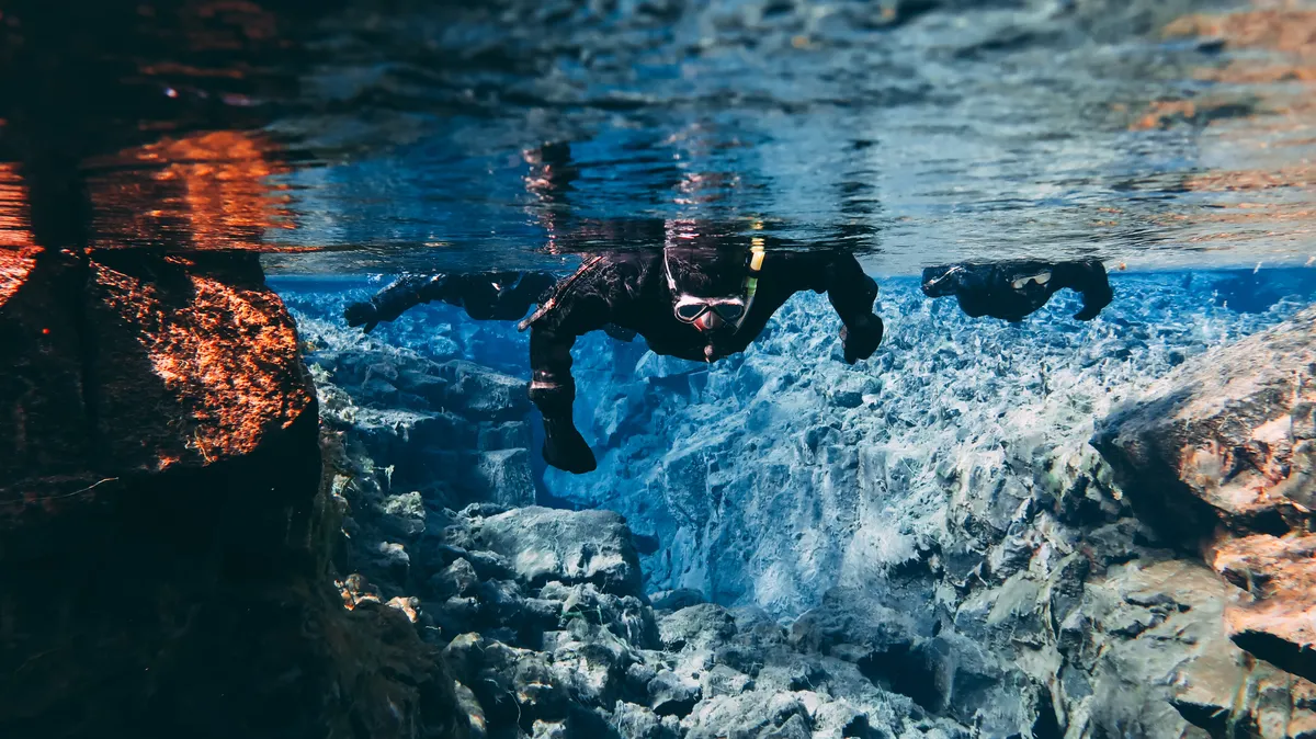 Aventureros haciendo esnórquel en las aguas cristalinas entre las placas tectónicas de Islandia, con visibilidad ampliada por la luz del verano de julio.