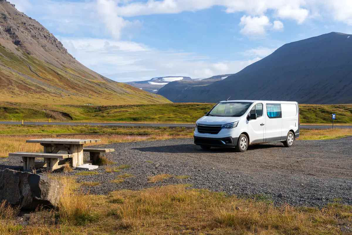 Una campervan blanca estacionada en un &aacute;rea de descanso designada en Islandia, con monta&ntilde;as y un glaciar al fondo. Cumpliendo con las leyes de camping en Islandia, el veh&iacute;culo est&aacute; estacionado en un lugar autorizado para evitar multas y da&ntilde;os ambientales.