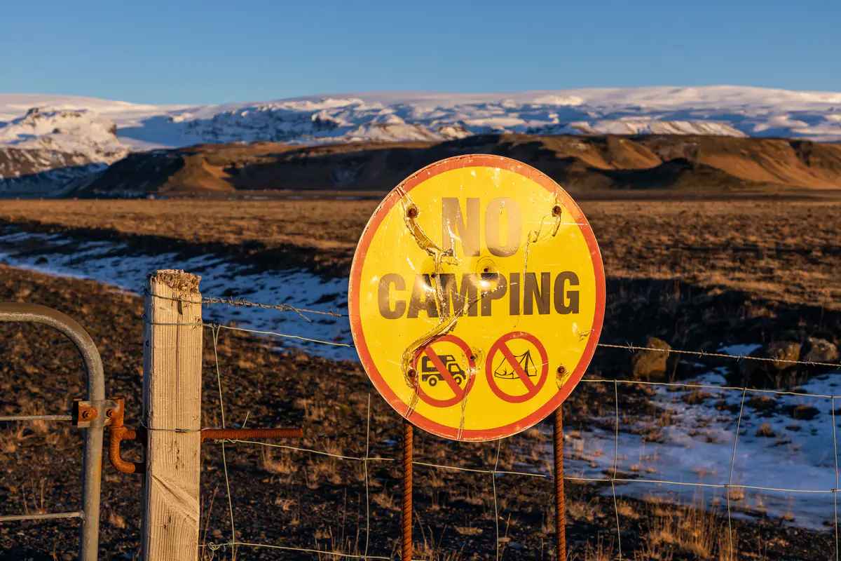 Un cartel de 'No acampar' en una zona vallada de Islandia, con monta&ntilde;as nevadas al fondo, destacando las estrictas regulaciones contra el camping salvaje.