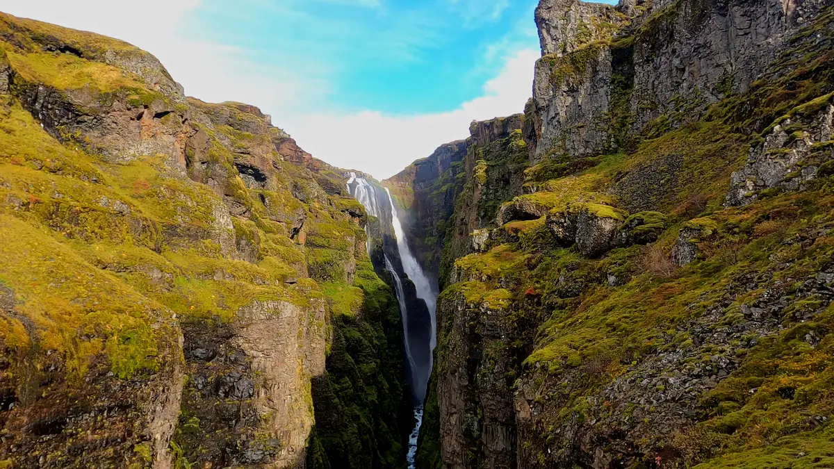 Majestuosa cascada en Islandia, cayendo entre imponentes acantilados cubiertos de musgo. Un destino perfecto para explorar en un viaje en autocaravana.