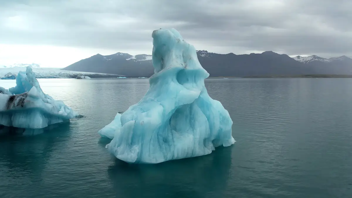 Impresionante iceberg flotando en la laguna glaciar Jökulsárlón en Islandia, con montañas nevadas de fondo. Un destino imprescindible en un road trip en autocaravana.