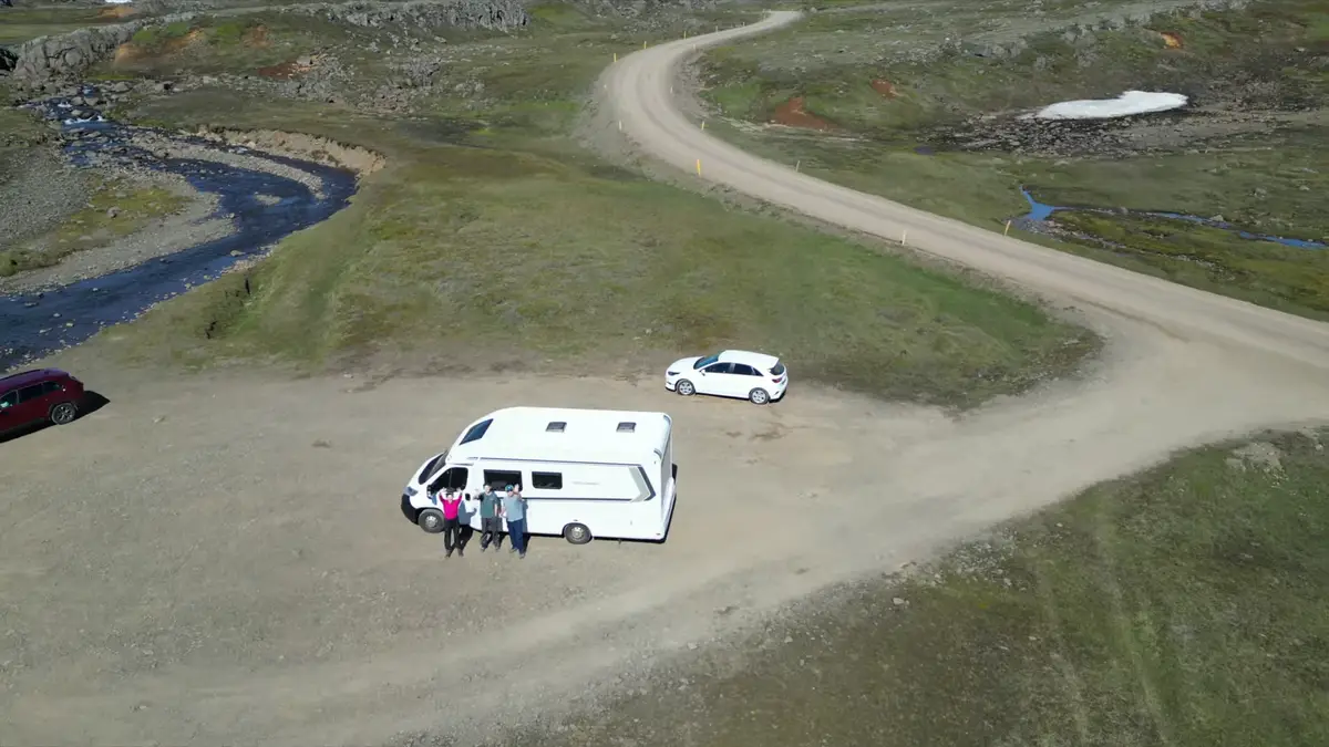 Autocaravana estacionada en un camino remoto de Islandia con un grupo de viajeros disfrutando del paisaje. La libertad de recorrer Islandia en camper permite explorar rincones fuera de las rutas turísticas.