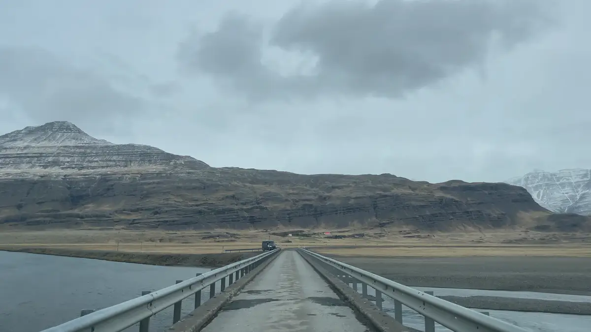Puente de un solo carril en Islandia con paisaje montañoso Vista de un puente de un solo carril en Islandia, rodeado de montañas con nieve en la cima y un cielo nublado. Este tipo de puentes son comunes en las carreteras islandesas y requieren precaución al conducir.
