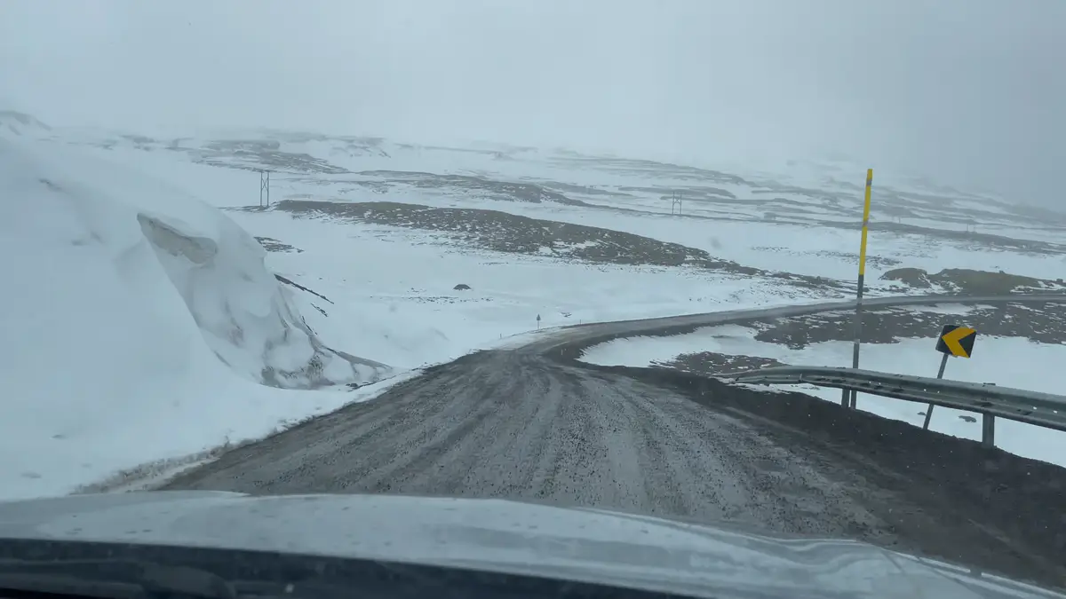 Carretera de montaña nevada en Islandia durante el invierno Vista de una carretera de grava en Islandia cubierta parcialmente de nieve, con curvas pronunciadas y señalización para condiciones invernales. Conducir en estas rutas requiere precaución, especialmente en invierno debido al hielo y la baja visibilidad.
