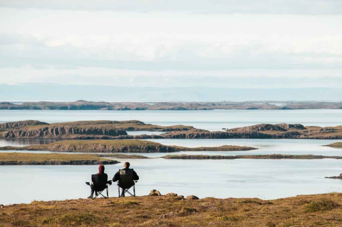 Espectáculo natural del verano en Islandia Una pareja sentada disfruta del espectáculo natural del verano en Islandia desde la distancia.