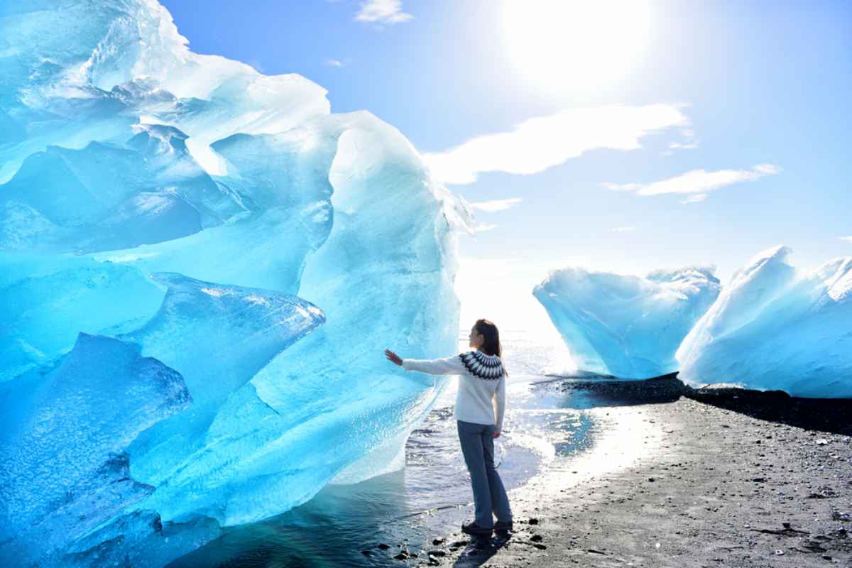 Bloques de hielo imponentes en Diamond Beach, Islandia Una mujer en miniatura toca con los dedos uno de los hermosos pero imponentes bloques de hielo en Diamond Beach, Islandia.