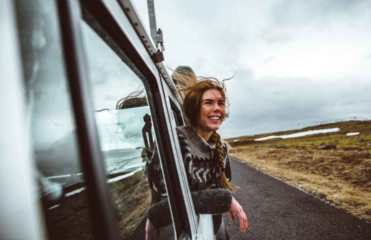Ráfagas de viento en Islandia Una mujer pelirroja saca la cabeza por la ventana de un vehículo en movimiento mientras el viento islandés sopla su cabello largo.