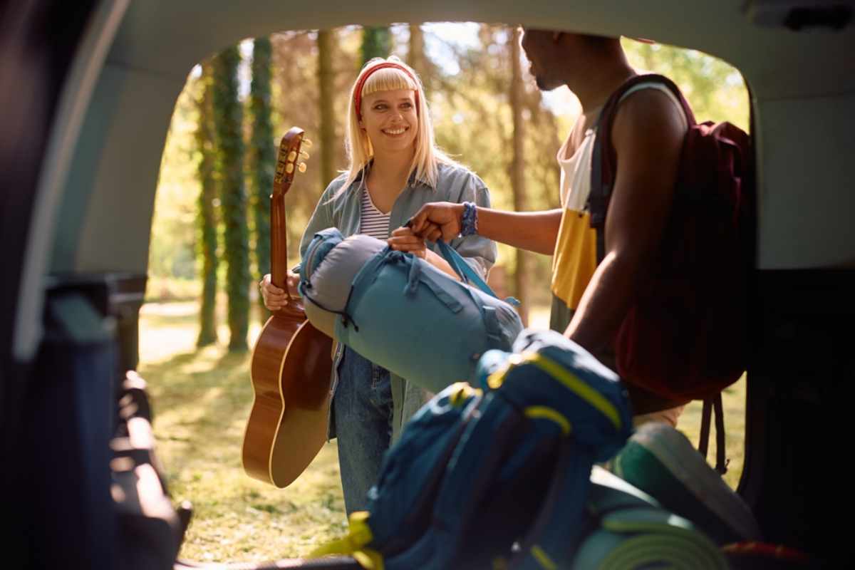 Pareja de turistas cargando sus mochilas y guitarra en la parte trasera de su camper
