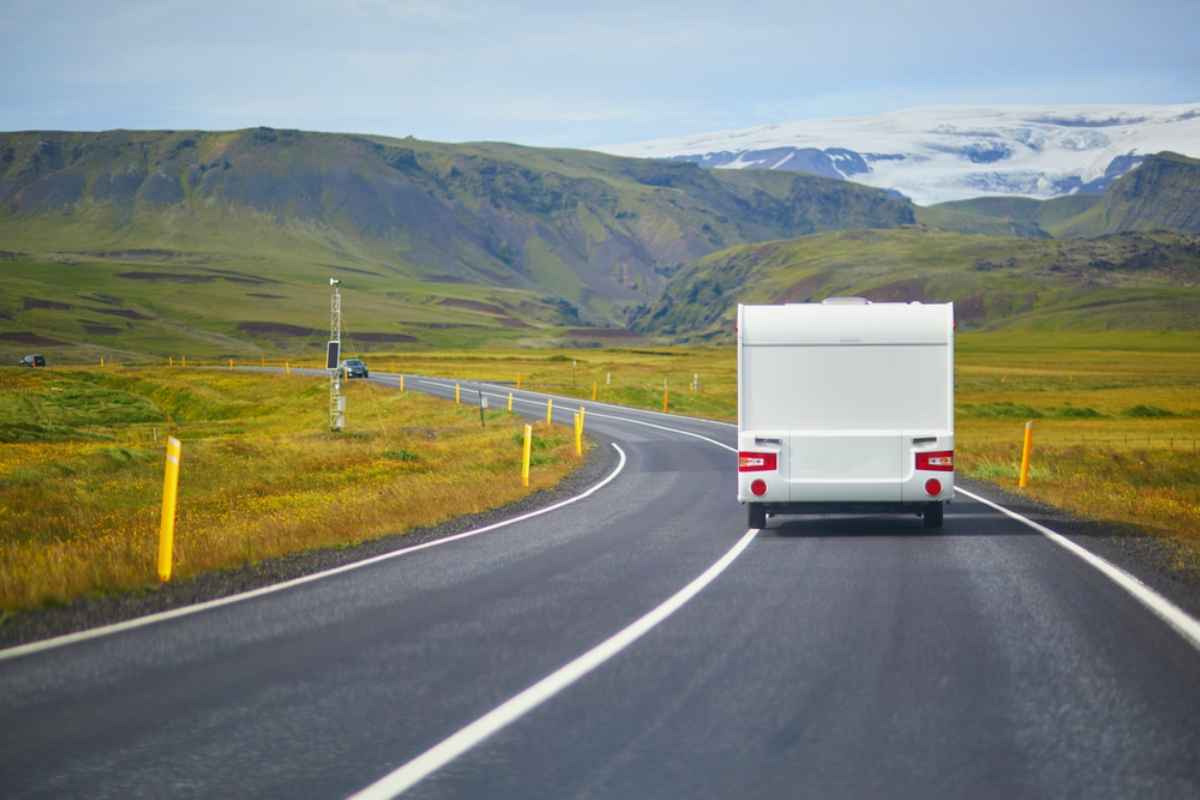 Un camping-car blanco circula libremente a lo largo de una carretera clara y colorida de la Ring Road islandesa.