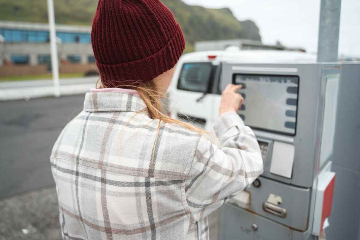 Una mujer con gorro de lana, de espaldas, manipulando una m&aacute;quina en una gasolinera de Islandia en el momento de pagar el repostaje.