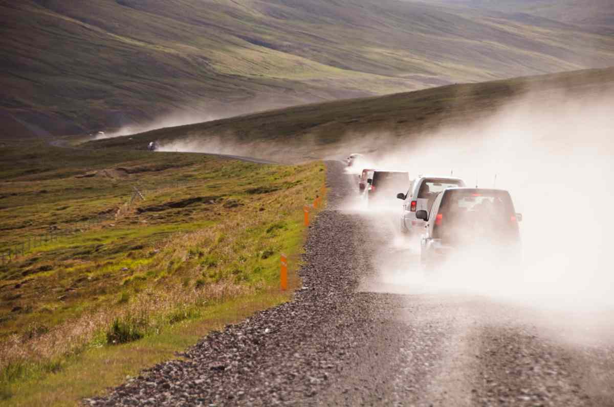Una fila de coches conduciendo por una carretera secundaria en Islandia dejando una nube de polvo tras ellos.