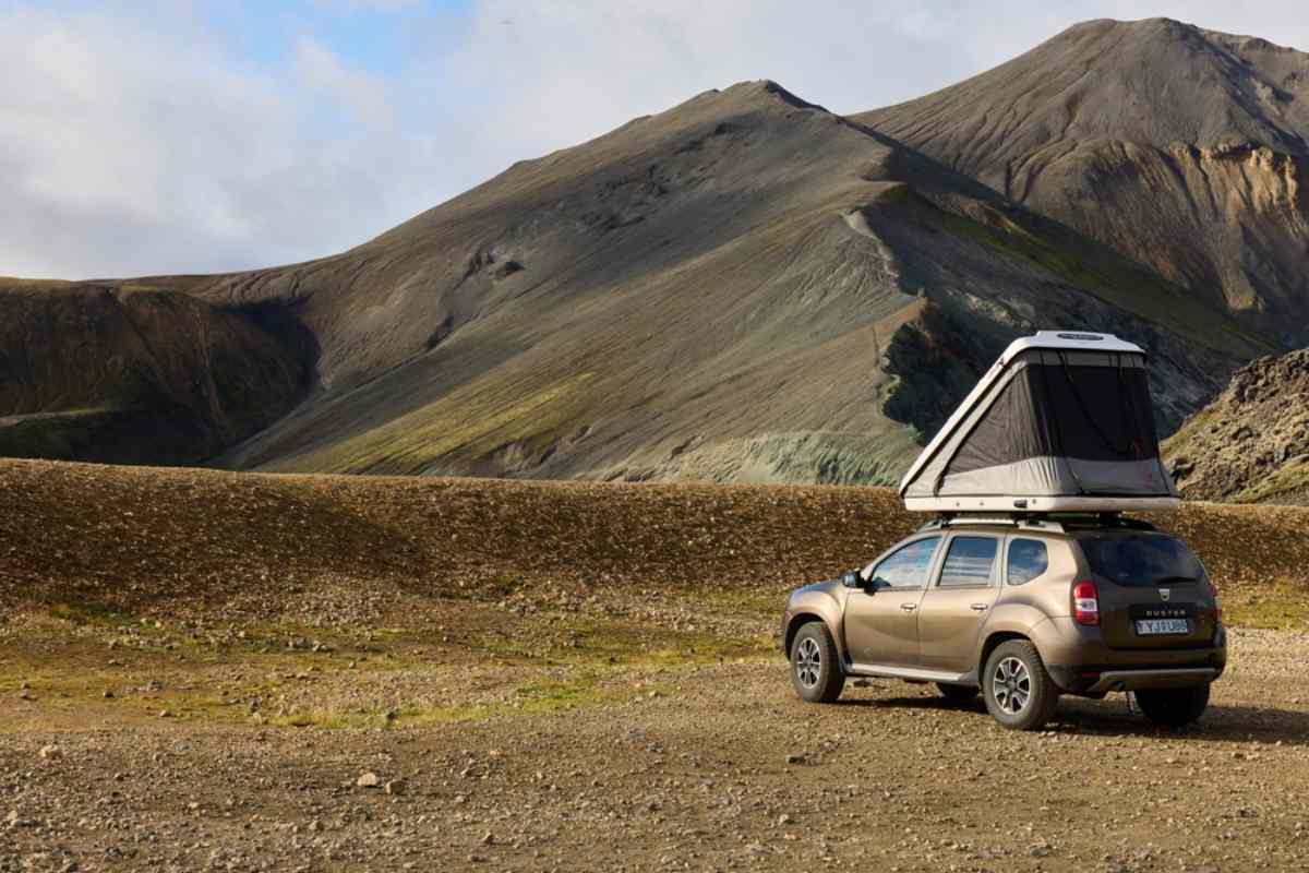 Un veh&iacute;culo Dacia Duster con tienda en el techo estacionado en un paisaje rocoso y des&eacute;rtico en Islandia.