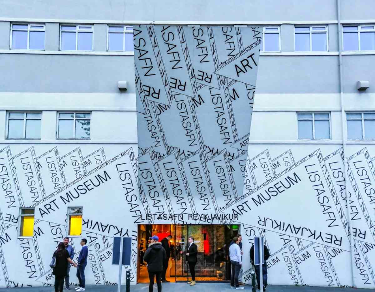 Fachada del museo de arte de Reikiavik con colores blanco y negro y inscripciones en el exterior, adem&aacute;s de la puerta de entrada con varias personas cruz&aacute;ndola.