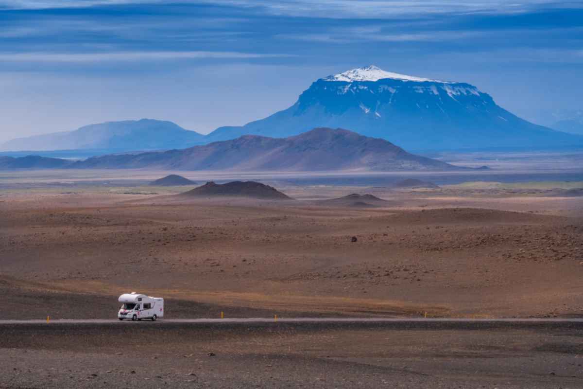 Una autocaravana blanca conduce por una carretera islandesa Una autocaravana blanca conduce por una carretera islandesa con una gran montaña nevada al fondo