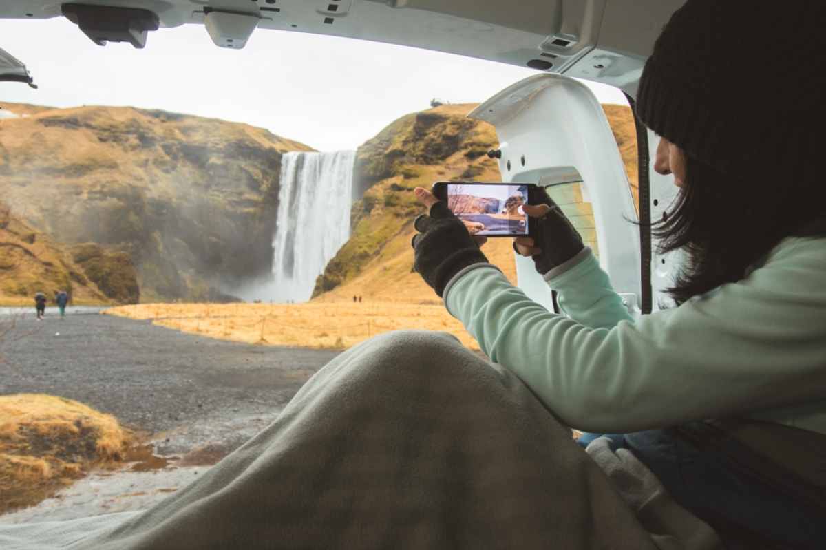 Turista tomando una foto de la cascada Skogafoss desde el interior de su acogedora autocaravana