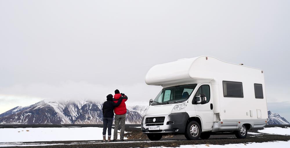 Dos viajeros abrazados junto a su autocaravana en un paisaje nevado de Islandia; nubes bajas y montañas, espíritu de aventura invernal.