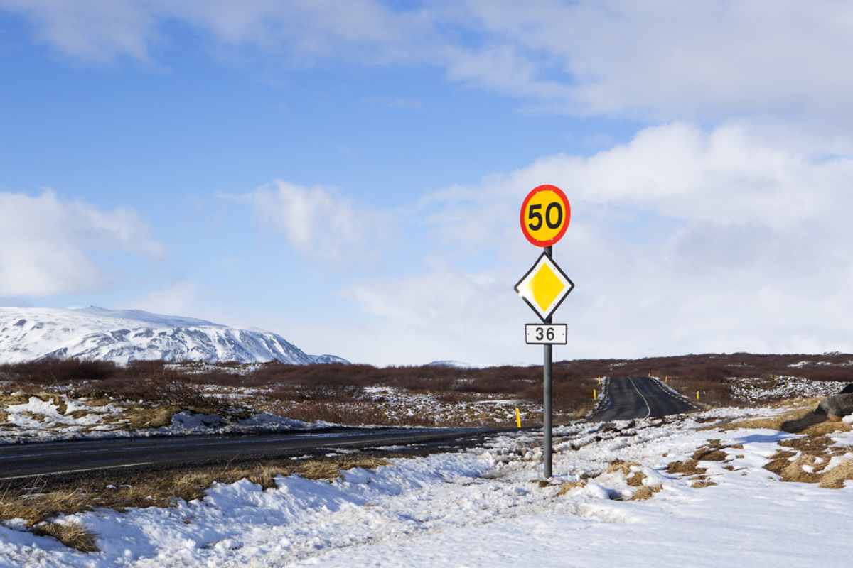 Carretera abierta en Islandia con montañas escarpadas de fondo y una señal de límite de velocidad