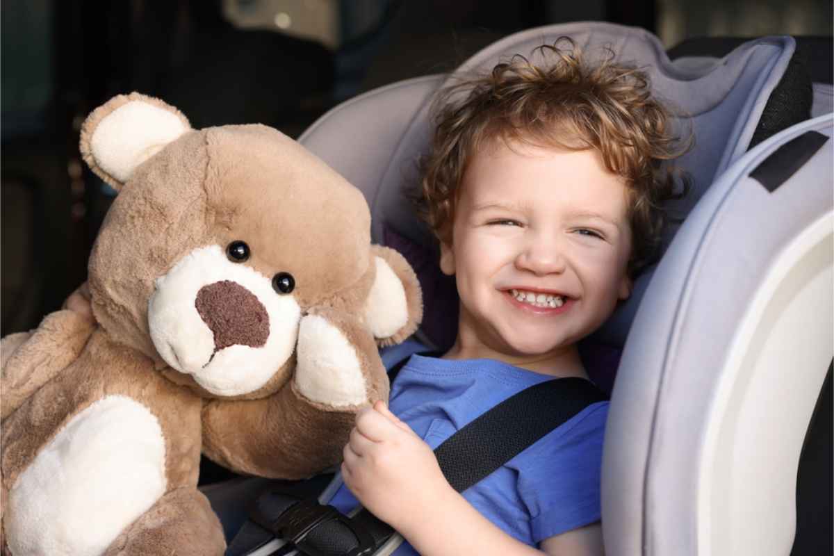 Niño feliz sentado en su silla infantil junto a un osito de peluche